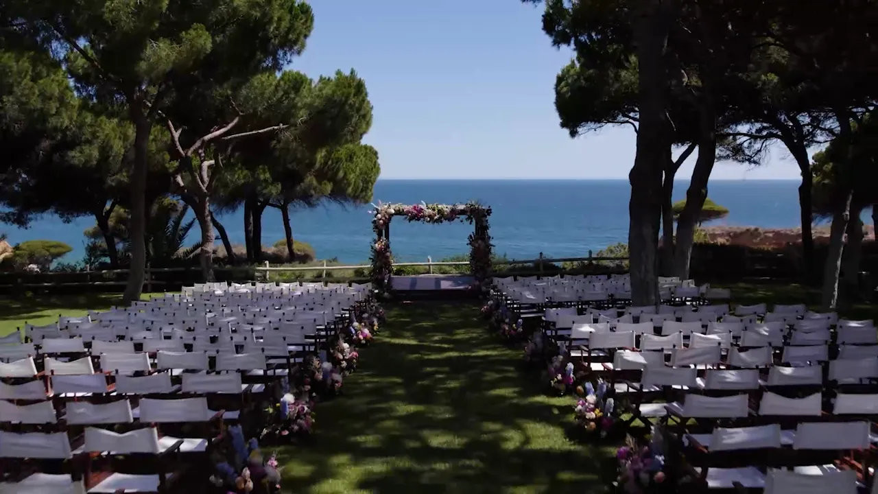 Ceremony under a floral arch among pine trees above the sea at Pine Cliffs, wedding film by VIP Weddings Films